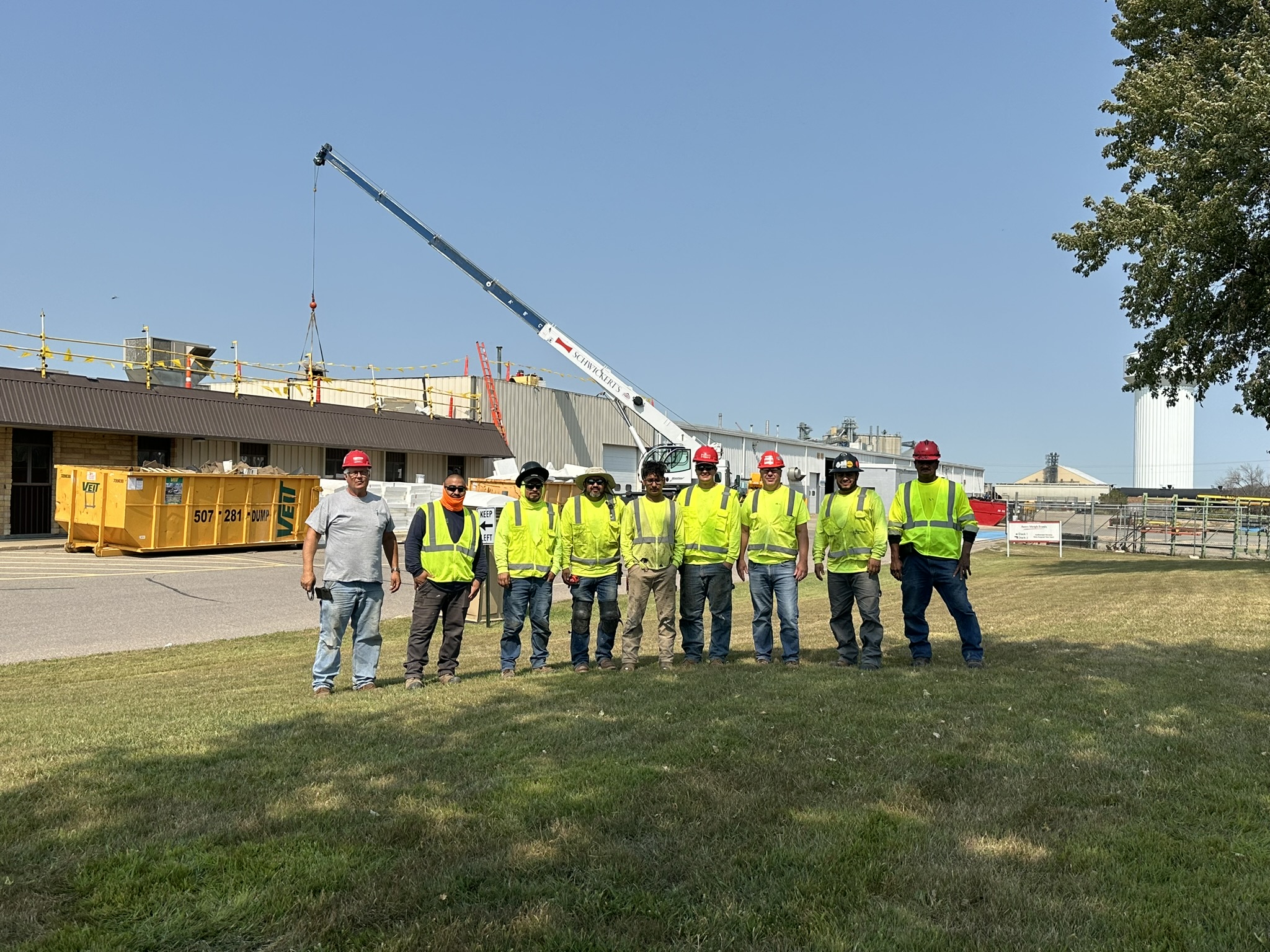 group picture of roofing crew in front of jobsite with crane in the background