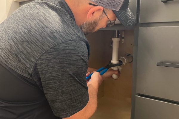 Schwickert's plumber tightening pipe underneath sink